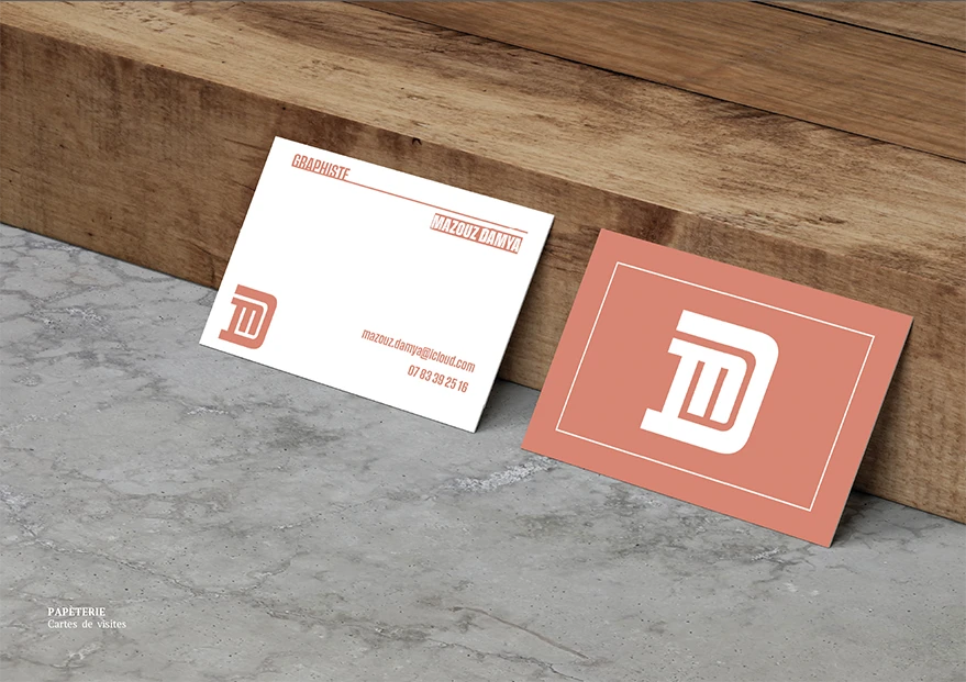 carte de visite pauser sur un rebord d'une table en bois avec le logo D et M en couleur corail